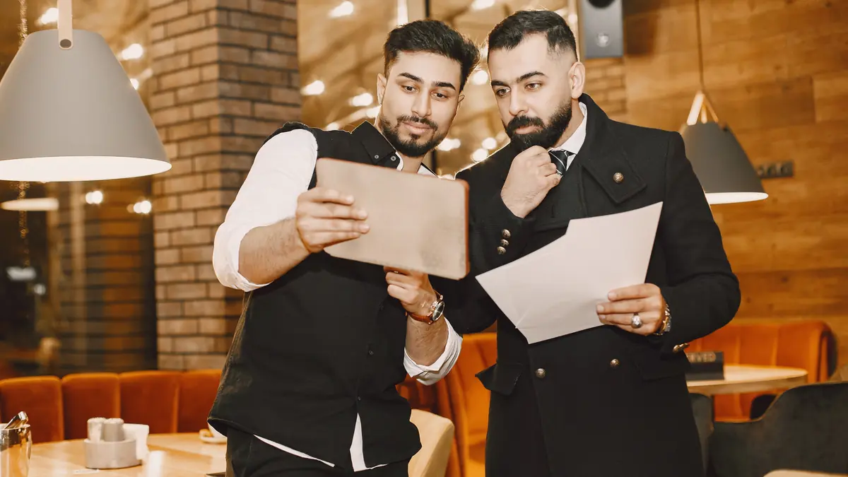 Two restaurant professionals reviewing documents and a tablet.