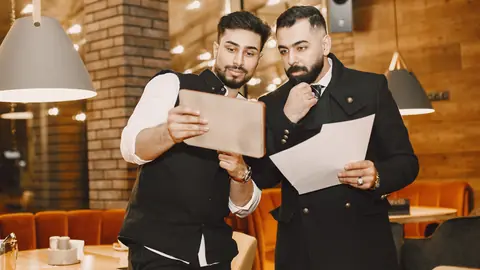 Two restaurant professionals reviewing documents and a tablet.